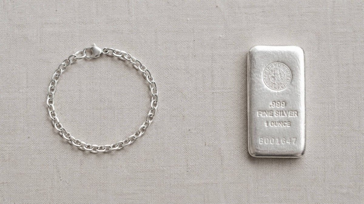 Silver bracelet and a 1-ounce .999 fine silver bullion bar side by side on a linen surface — illustrating the difference between silver jewelry and silver bullion as investments