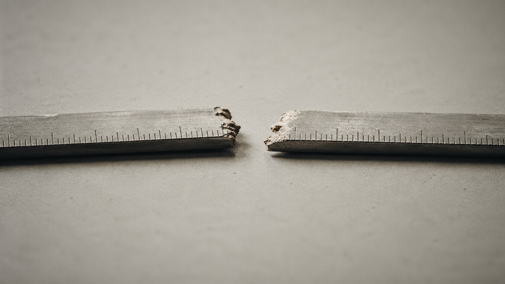 A wooden ruler snapped in two, photographed on a grey surface — illustrating the broken inflation measurement framework facing the incoming Federal Reserve Chair.